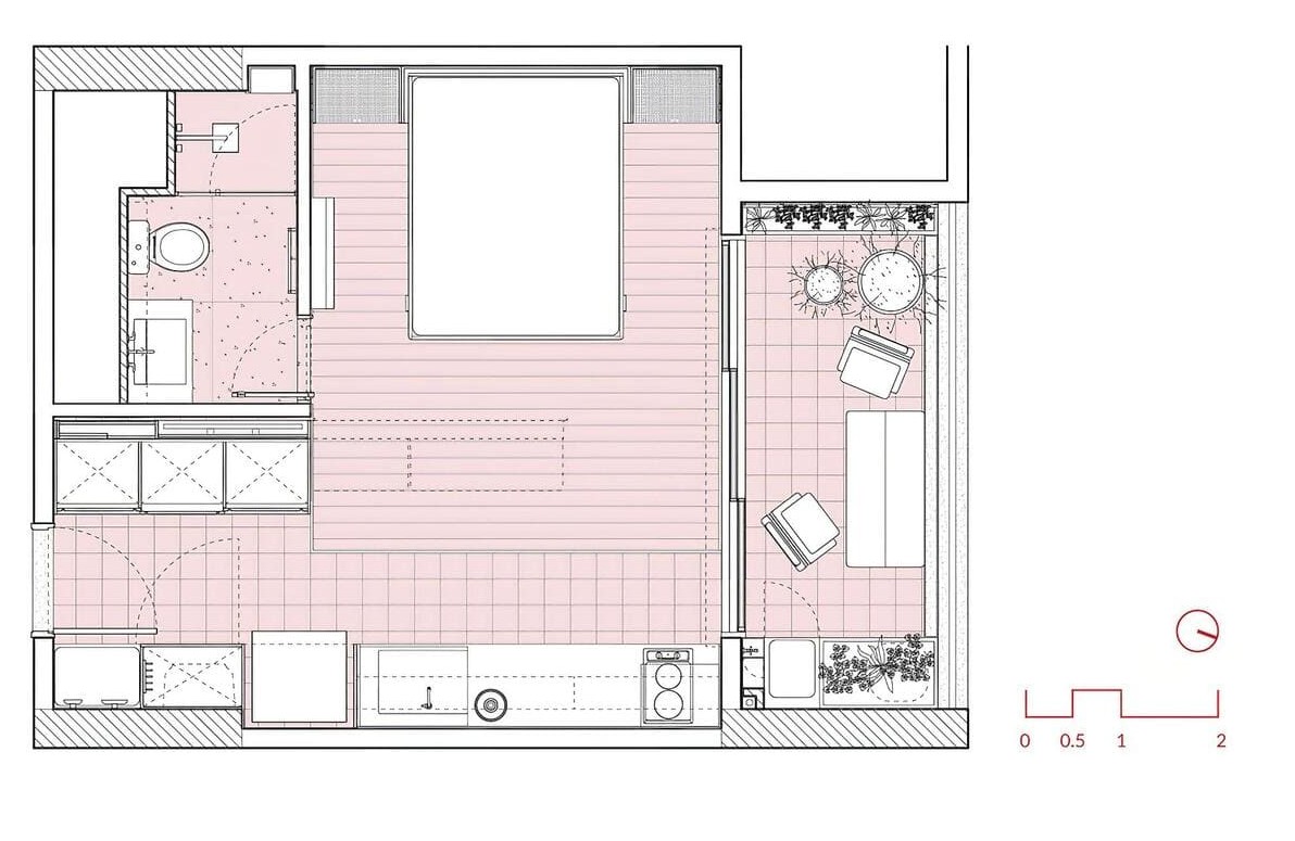 Floor plan of a small apartment showing a bedroom with a double bed, a bathroom, a kitchen, and a living area with a sofa, chairs, a TV, and a balcony with potted plants. A scale and compass are in the corner.
