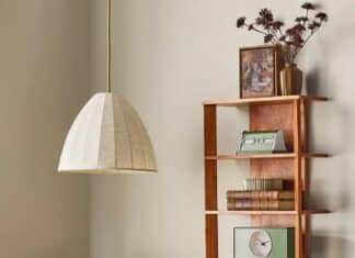 A cozy desk setup with a wooden desk, a fabric pendant lamp from the Hearth & Hand Magnolia Collection at Target, a vintage radio, and books. A wooden wall shelf displays more books, a clock, photo frame, and dried flowers in a vase.