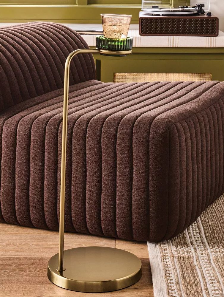 A modern brass side table from the Magnolia Collection holds a glass on a ribbed brown sofa, with a turntable and decor in the background. Warm tones and contemporary Target furnishings sit on a hardwood floor with a woven rug.