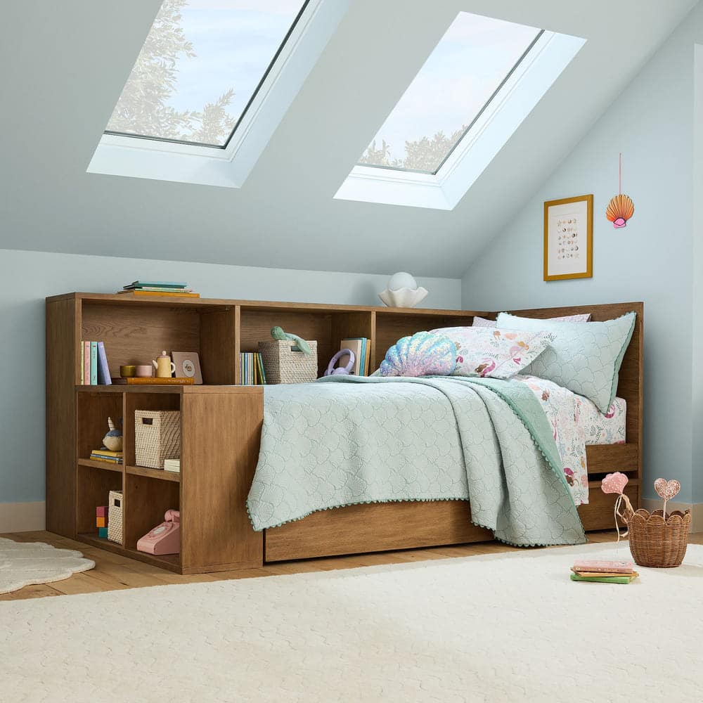A cozy bedroom with a wooden storage bed featuring built-in shelves, pastel bedding, and pillows. Skylights let in natural light, and the walls are light blue. Books, baskets, and decorative items fill the shelves.