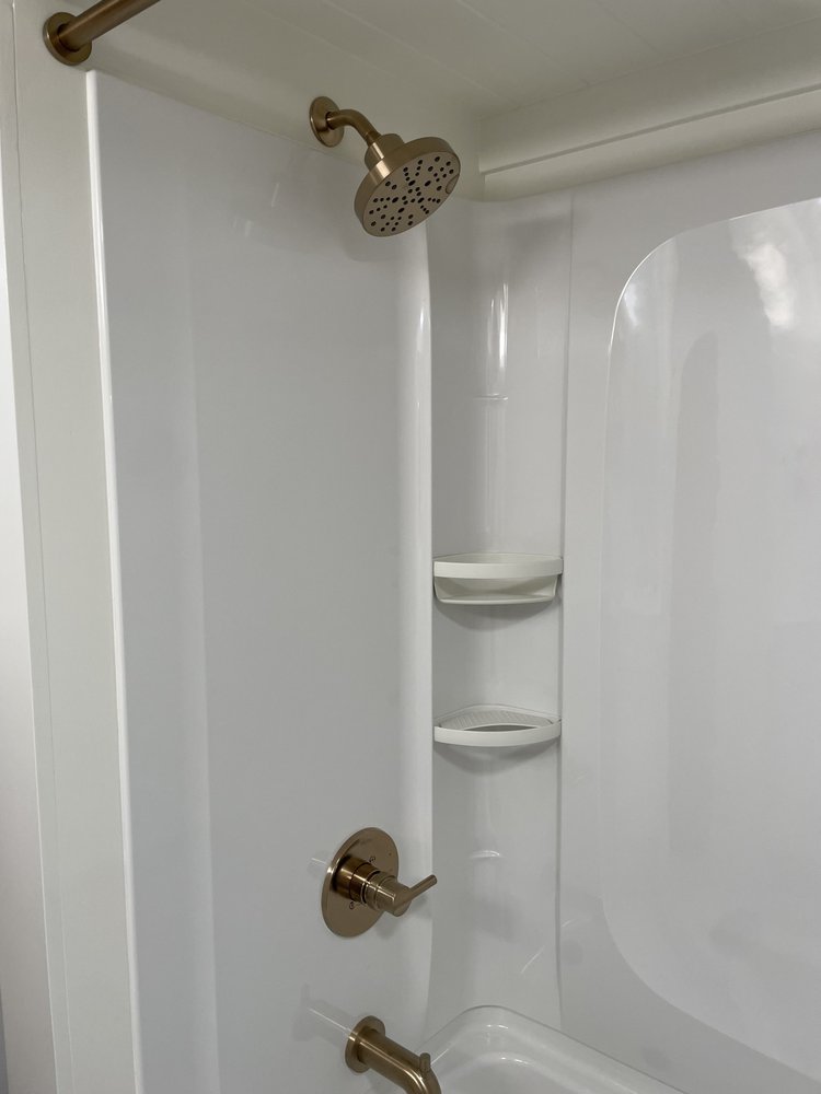 A clean white bathtub and shower with gold fixtures, including a round showerhead and faucet, plus built-in corner shelves—perfectly designed for a stylish tiny house.